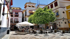 Un área de café al aire libre con mesas y sillas, rodeada de edificios con balcones y detalles decorativos.