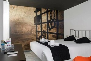 A hotel room with a bed, a desk with a phone and a glass, and a wall with a textured design. - Casual Sevilla Don Juan Tenorio (Seville)