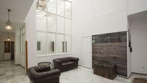 Una habitación amplia con un gran ventanal, un sofá de cuero, un banco de madera y una puerta con paneles rústicos.