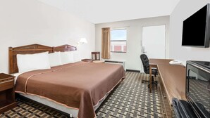 A hotel room with a large bed, a desk, a chair, a television, and a window with curtains. - Knights Inn Slaton (Slaton)
