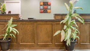 A reception area with a wooden counter, potted plants, and a decorative wall piece. - Knights Inn Slaton (Slaton)