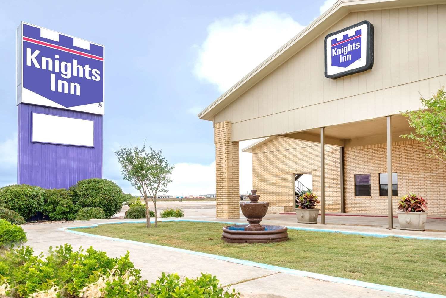 Um hotel Knights Inn com uma placa grande, um edifício de tijolos e uma área de entrada com paisagismo.