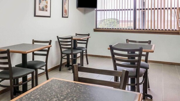 A room with a dining area featuring tables and chairs, a TV mounted on the wall, and a window with vertical blinds. - Knights Inn Slaton (Slaton)