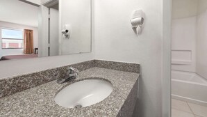 A bathroom with a granite countertop sink, a mirror, a handheld hair dryer, and a shower area. - Knights Inn Slaton (Slaton)
