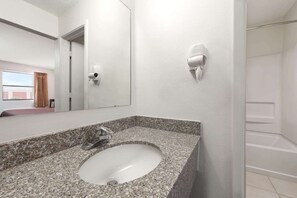 A bathroom with a granite countertop sink, a mirror, a handheld hair dryer, and a shower area. - Knights Inn Slaton (Slaton)