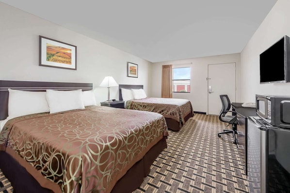 A hotel room with two beds, a desk with a TV, a window, and artwork on the walls.