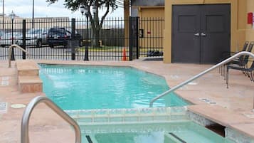Una piscina rectangular con una escalera metálica y escalones, rodeada por una valla y un edificio con una puerta.