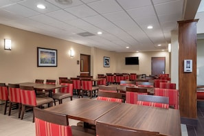 Un espace de restauration d’hôtel comprenant plusieurs tables et des banquettes, équipé de téléviseurs fixés au mur et d’un éclairage d’ambiance.