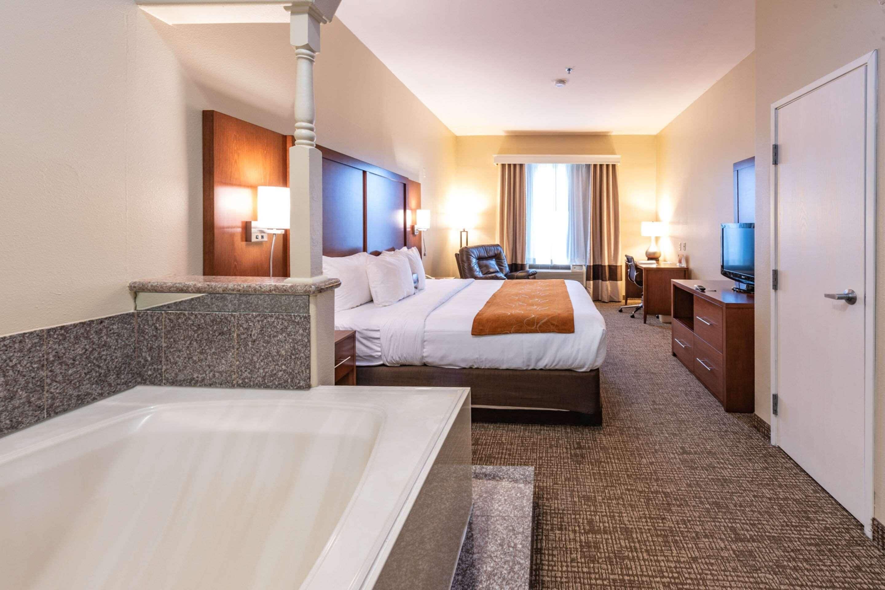 A hotel room with a large bed, a separate sitting area with a chair, a desk, a television, and a bathroom with a bathtub.