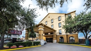Entrada de hotel con un letrero de Comfort Suites, zona de estacionamiento techada y cielo despejado.
