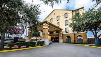 Entrada de hotel con un letrero de Comfort Suites, zona de estacionamiento techada y cielo despejado.