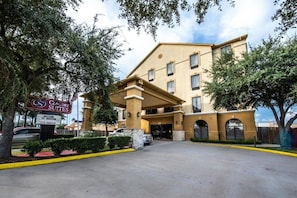 A hotel entrance with a sign for Comfort Suites, a covered parking area, and a clear sky.
