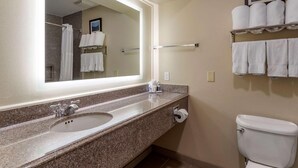 Un baño con lavamanos, espejo, inodoro y perchero para toallas.