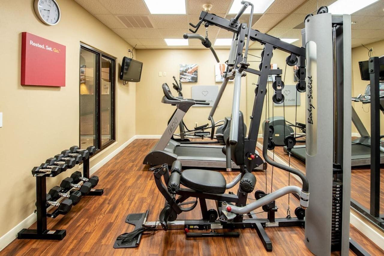 Uma academia com equipamentos de ginástica, um relógio e um letreiro motivacional.