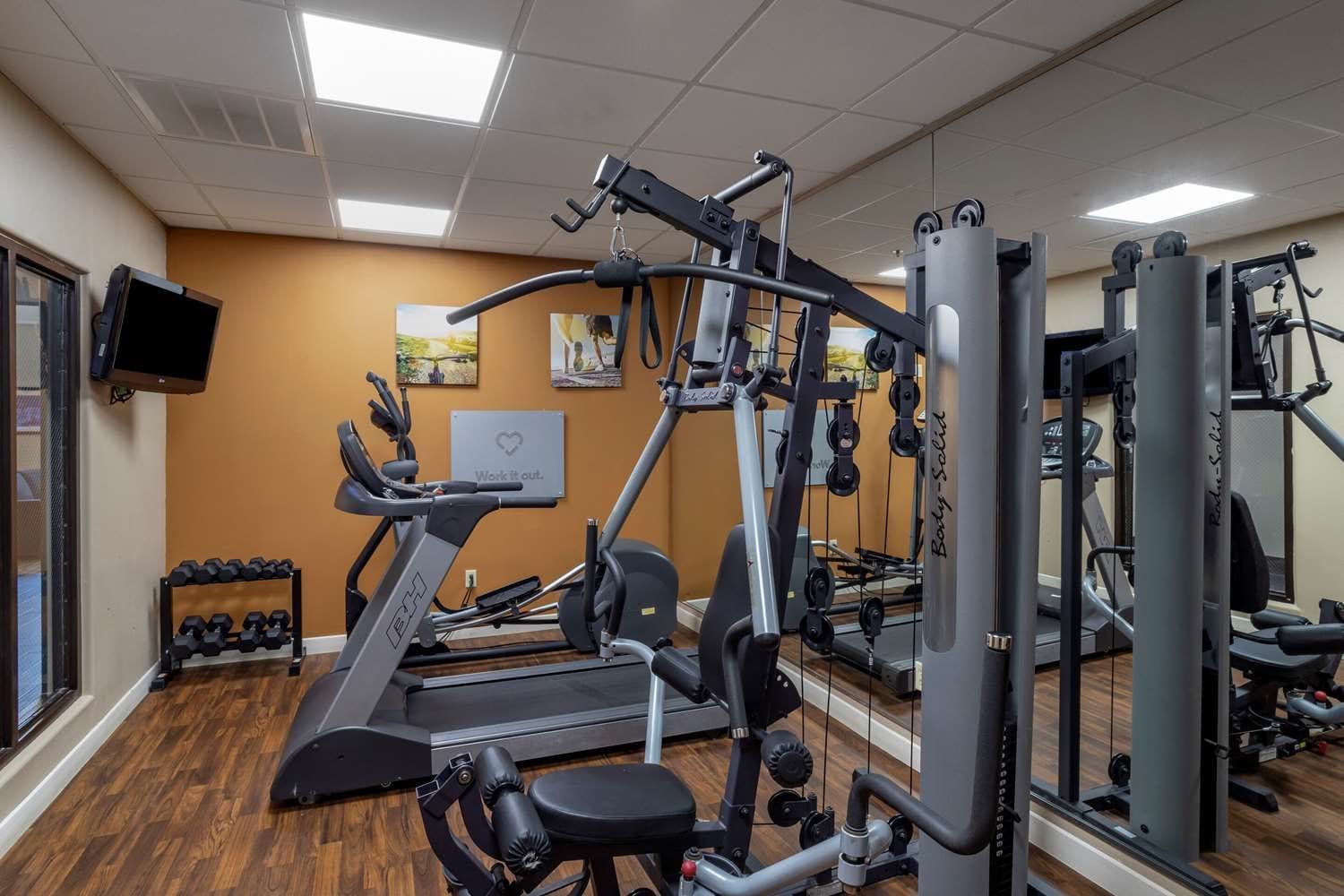 A gym with cardio machines, weightlifting equipment, and a television on the wall.