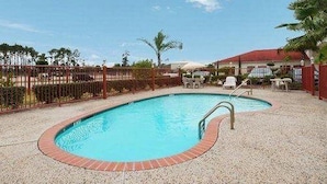 A swimming pool with a brick edge, surrounded by a fence, and a building with a red roof in the background. - Red Roof Inn & Suites Houston Humble/iah Airport (Humble)