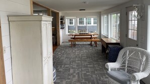 A kitchen with a wooden table and bench, a wicker chair, and a white cabinet.