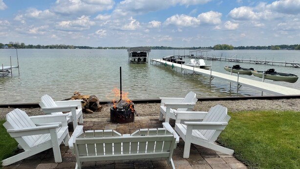 A lakeside patio with Adirondack chairs, a fire pit, and docked kayaks.