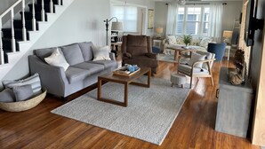A modern living room with a staircase, a brown leather armchair, a grey sofa, and a wooden coffee table.