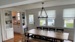 A dining area with a wooden table and benches, white cabinets, and a view of parked cars outside.