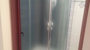 A glass-enclosed shower stall with a white tiled wall and a decorative tile border. - Marack2 (Nessebar)