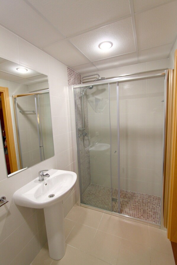 A bathroom with a glass-enclosed shower, a sink, and a mirror. - Roca Hostal (Sant Antoni de Portmany)