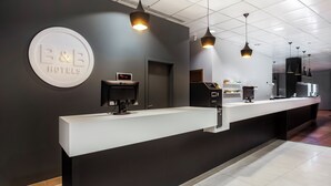 Een hotel receptie met een modern design, met een receptiebalie, een digitale klok en een koffieapparaat.