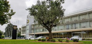 A modern hotel with a large tree in front, a parking area, and a clear sky. - B&B Hotel Cantanhede Coimbra (Cantanhede)