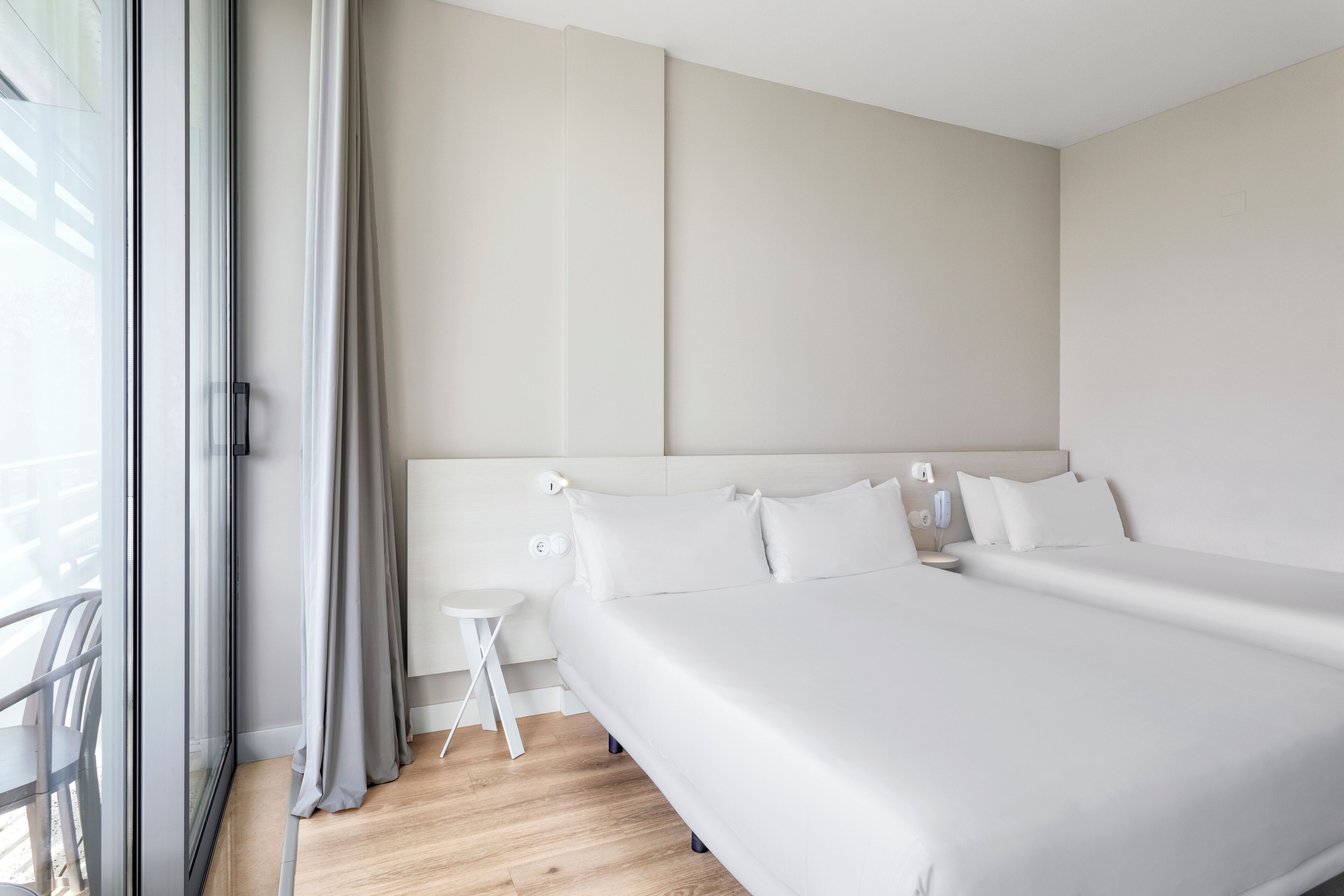 Camera d'albergo moderna con un letto grande, un comodino e vista sull'esterno tramite una porta scorrevole in vetro.