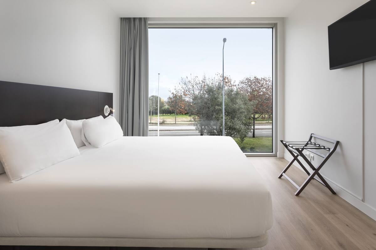 Une chambre moderne avec un grand lit, une vue sur un parc et un téléviseur fixé au mur.