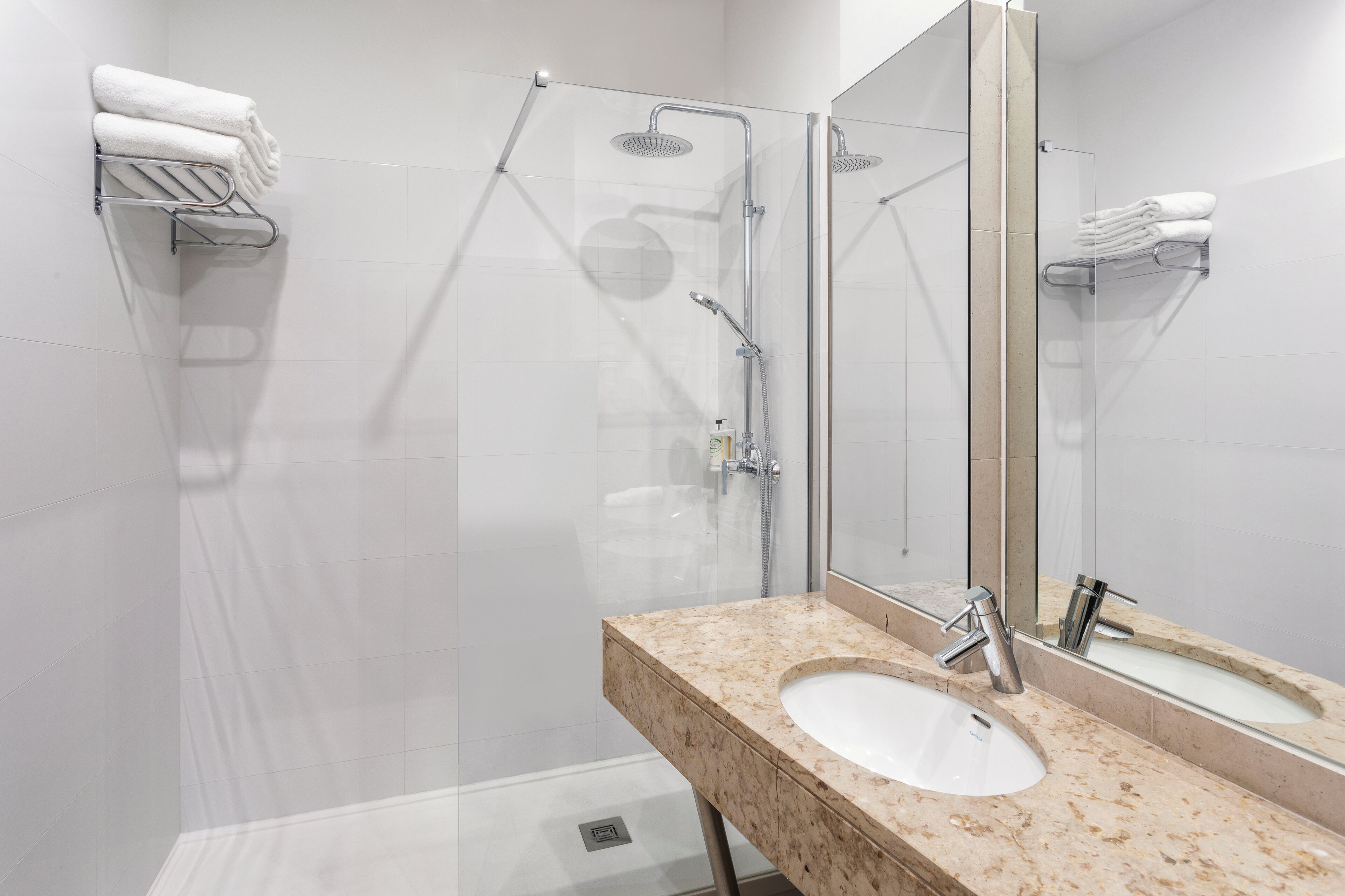 Un baño moderno con ducha envuelta en vidrio, lavamanos de mármol y un espejo grande.