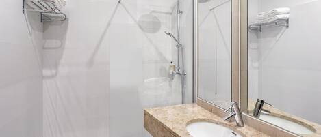 Un baño moderno con ducha envuelta en vidrio, lavamanos de mármol y un espejo grande.
