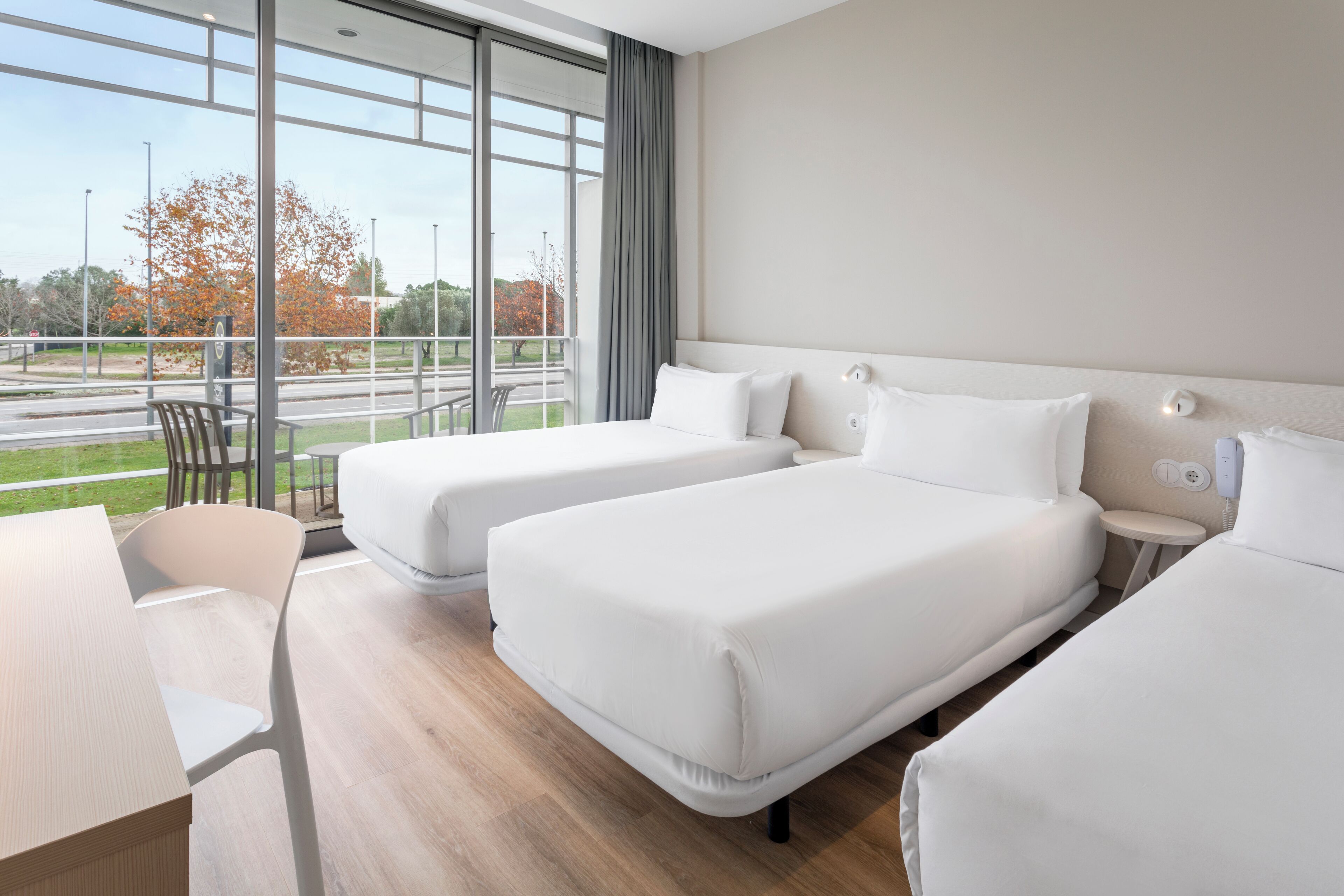Habitación de hotel con dos camas, un escritorio y vistas al exterior.