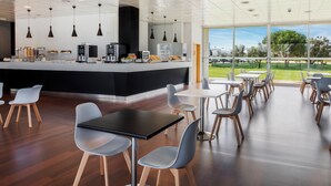 Een modern café met een centraal bedieningspunt, een zithoek en grote ramen met uitzicht op het omliggende landschap.