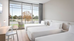 Een hotelkamer met twee bedden, een bureau, een stoel en een groot raam met uitzicht op de omgeving.