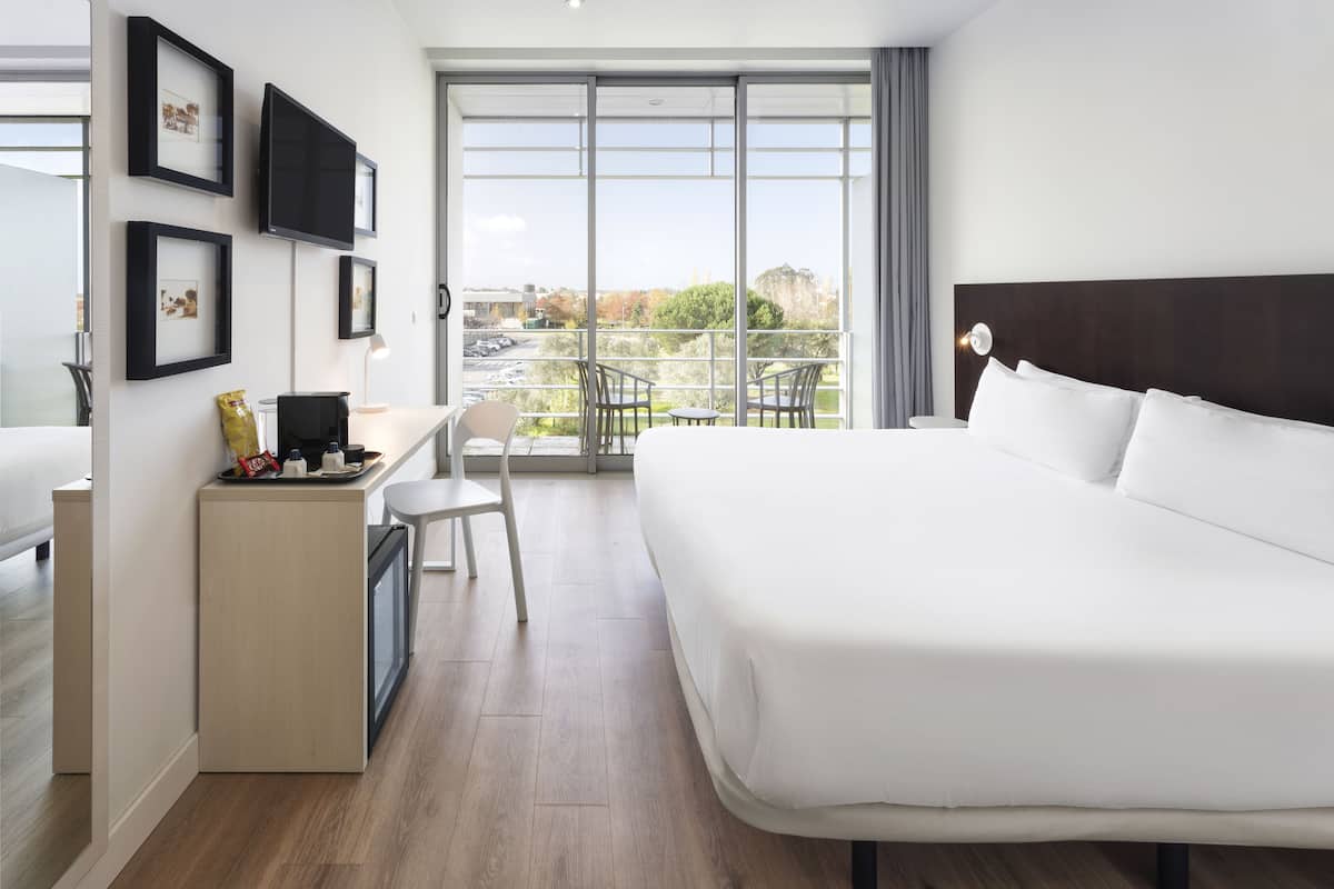 Une chambre d’hôtel moderne dotée d’un grand lit, d’un bureau avec une chaise, d’une petite table et d’un balcon avec des chaises.