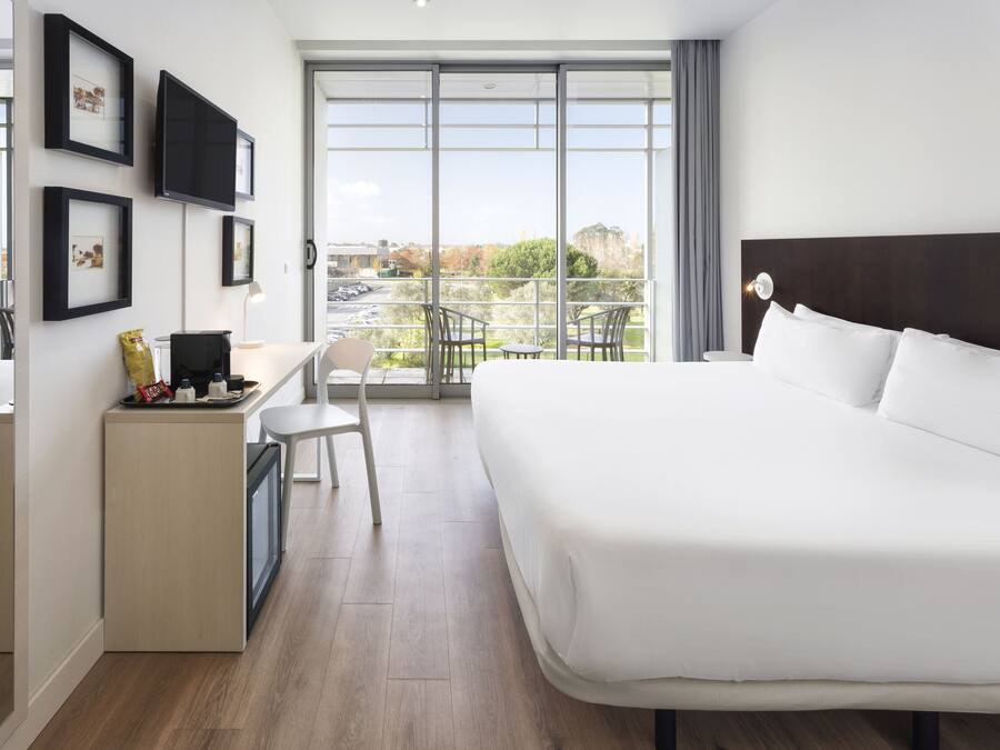 Una camera d'albergo moderna con un letto grande, una scrivania con una sedia, un tavolino e un balcone con sedie.