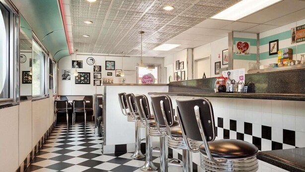 A diner interior with a checkered floor, bar stools, and a counter with a menu. - Travelodge by Wyndham Dunsmuir (Dunsmuir)