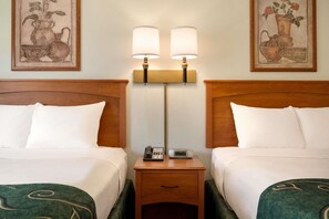Quarto de hotel com duas camas, uma mesa de cabeceira com telefone e relógio, e duas luminárias de parede.