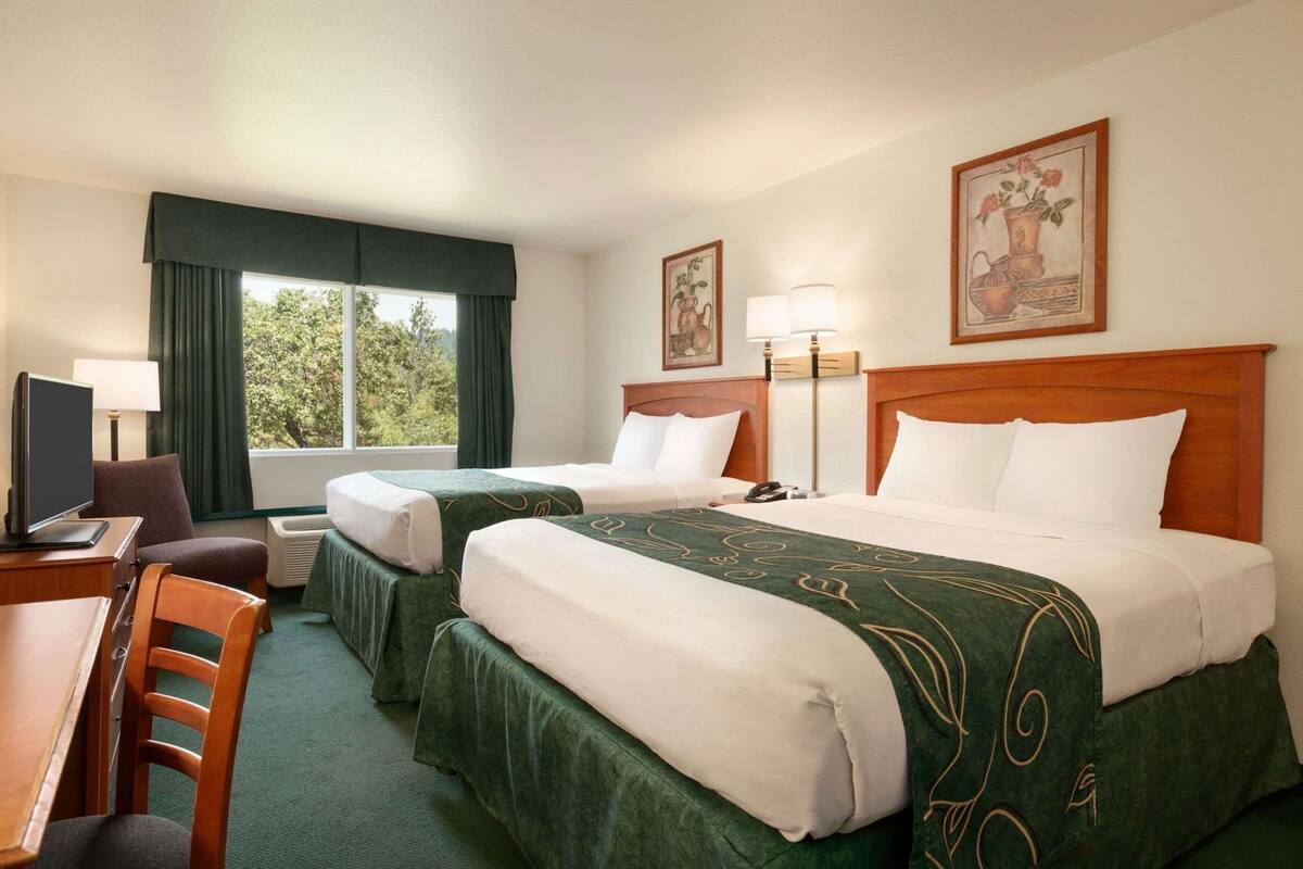 Una habitación de hotel con dos camas, un escritorio con silla, televisión y ventana con cortinas.