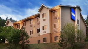 A multi-story hotel with a modern design, featuring a prominent blue sign on the corner, multiple windows on each floor, and a landscaped front yard with trees. - Travelodge by Wyndham Dunsmuir (Dunsmuir)