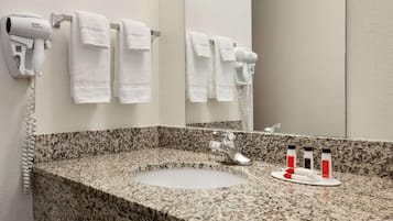 Une salle de bain dotée d’un comptoir en granit, d’un lavabo, d’un miroir et de deux sèche-cheveux fixés au mur.