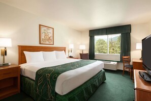 Quarto de hotel com cama, mesas de cabeceira, escrivaninha com cadeira, televisão e janela com cortinas.