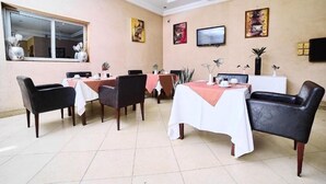 Comedor con mesas dispuestas para cuatro, sillas, un televisor y obras de arte en las paredes.