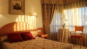 A hotel room with a bed, a desk, a chair, a lamp, a vase with flowers, and curtains. - Cabo Festinanza (Sanxenxo)