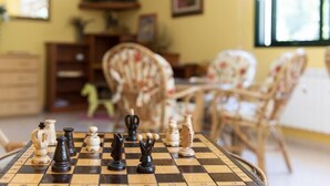 A chessboard with pieces in a room with a television, wooden furniture, and a window. - Cabo Festinanza (Sanxenxo)