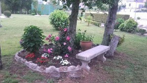 A garden with a stone bench, flowering plants, and a tree. - Cabo Festinanza (Sanxenxo)