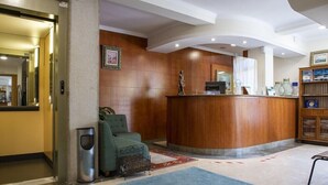 A reception area with a wooden reception desk, a green armchair, a trash bin, and a patterned rug. - Cabo Festinanza (Sanxenxo)
