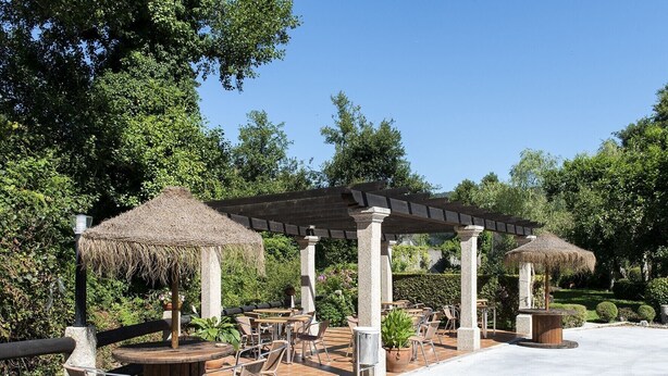 An outdoor patio area with thatched-roof pergolas, wooden tables, and chairs. - Cabo Festinanza (Sanxenxo)