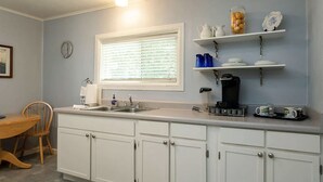 A kitchen with white cabinets, a sink, a coffee maker, and shelves with kitchenware.